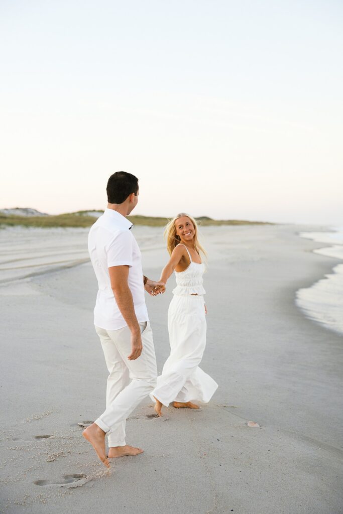 An engaged couple walks along the beach at Island Beach State Park.