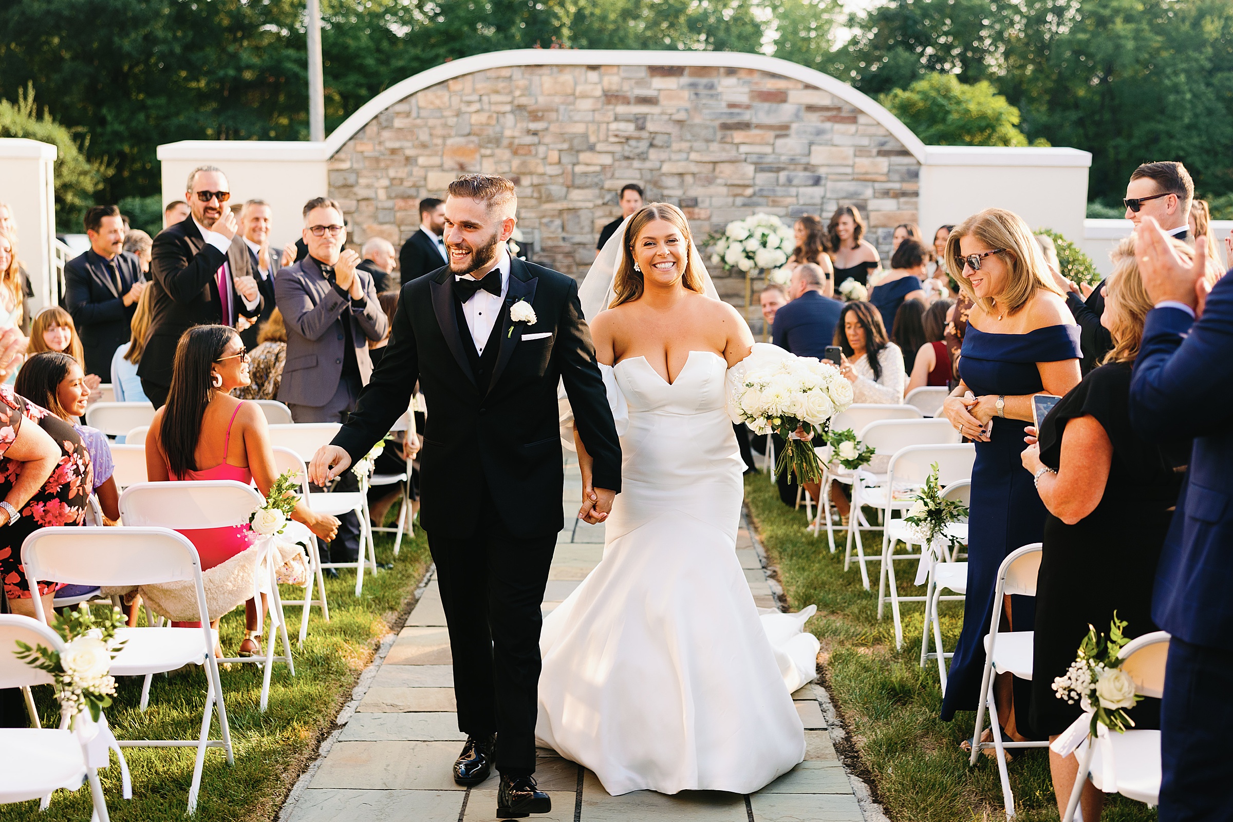 A couple comes down the aisle in their outdoor ceremony at the Mansion at Mountain Lakes