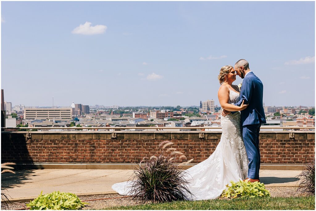 A bride and groom pose on a rooftop with the Baltimore skyline behind them.