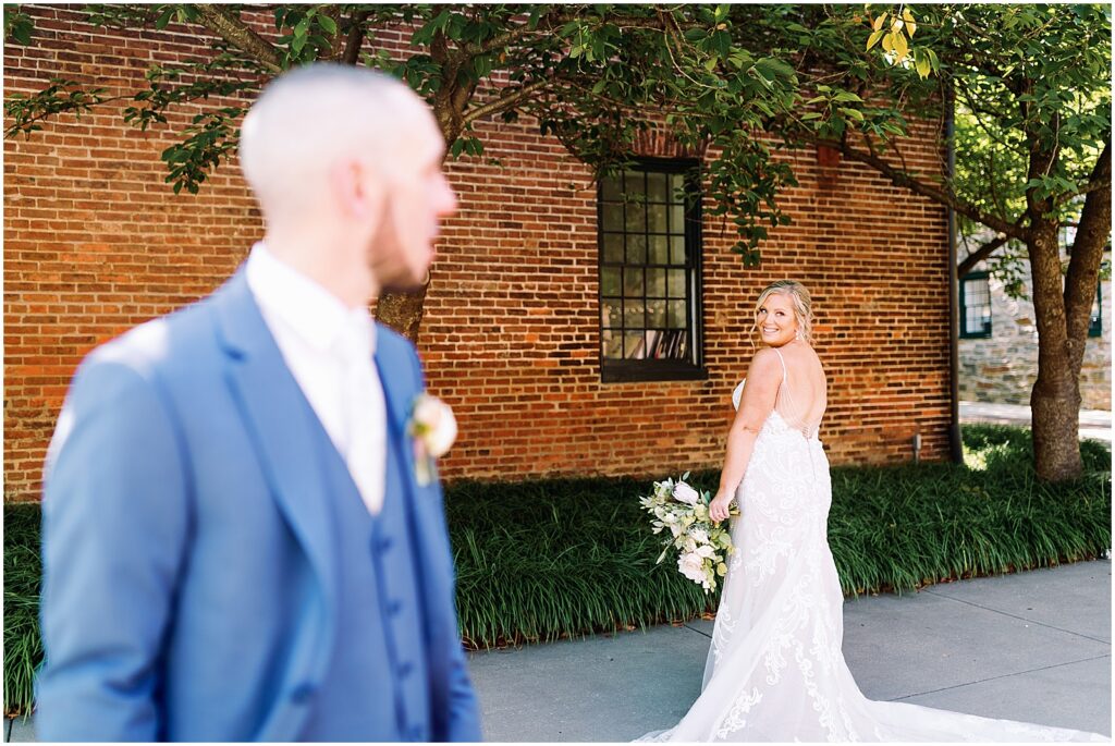 A groom looks across a courtyard at a Baltimore wedding venue to a bride who is posing for a wedding portrait.