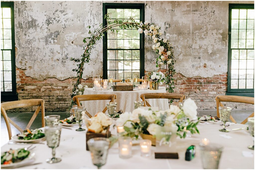 A floral arch sits behind a sweetheart table inside the wedding reception space at Mt Washington Mill Dye House.