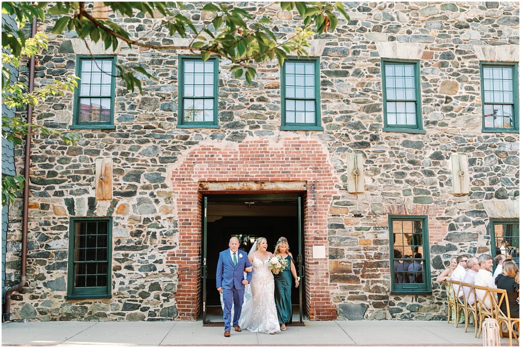 A bride's parents walk with her out of a door into the courtyard of the Mt Washington Mill Dye House.