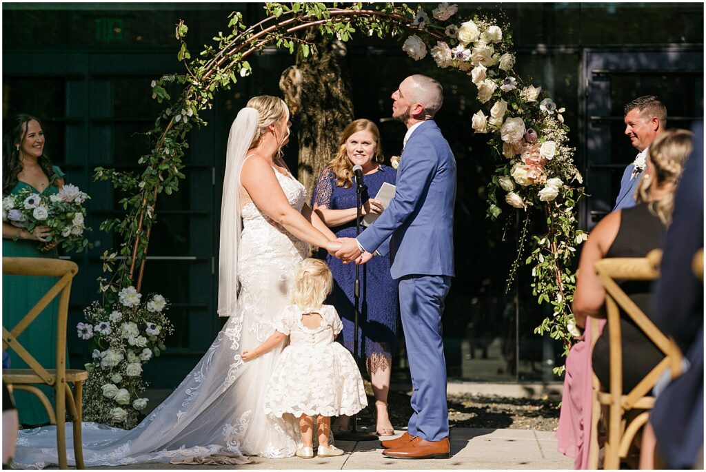 A bride and groom hold hands beneath a floral wedding arch.