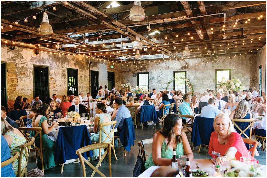 Wedding guests eat dinner at round tables in the reception space of Mt Washington Mill Dye House.