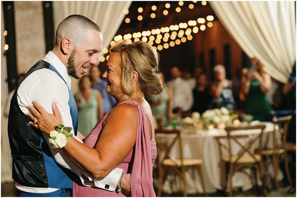 A groom and his mother smile at each other while they dance.