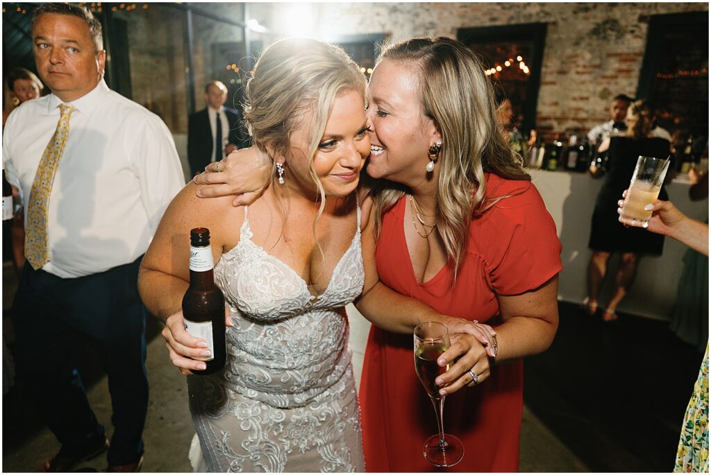 A wedding guest puts her arm around a bride and speaks into her ear.
