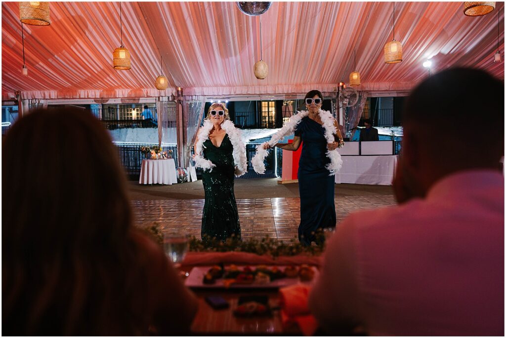 Two women with white feather boas dance in a reception tent.