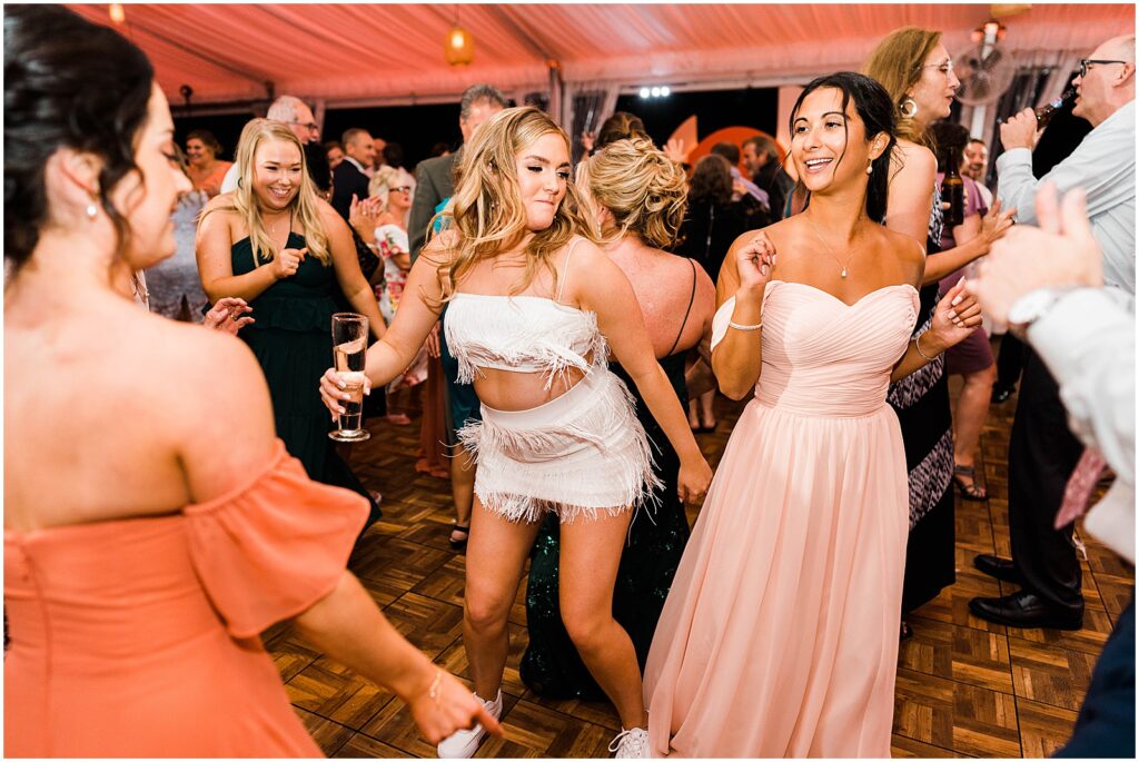 A bride dances with women in orange and pink bridesmaids dresses.