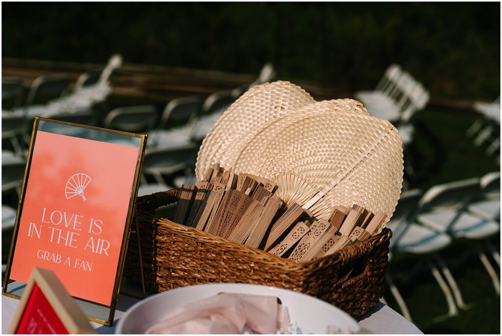 Wedding fans sit in a basket for a summer wedding ceremony.