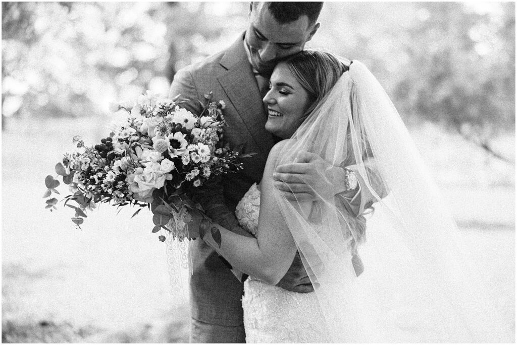 A bride holding a bridal bouquet embraces a groom at their first look.
