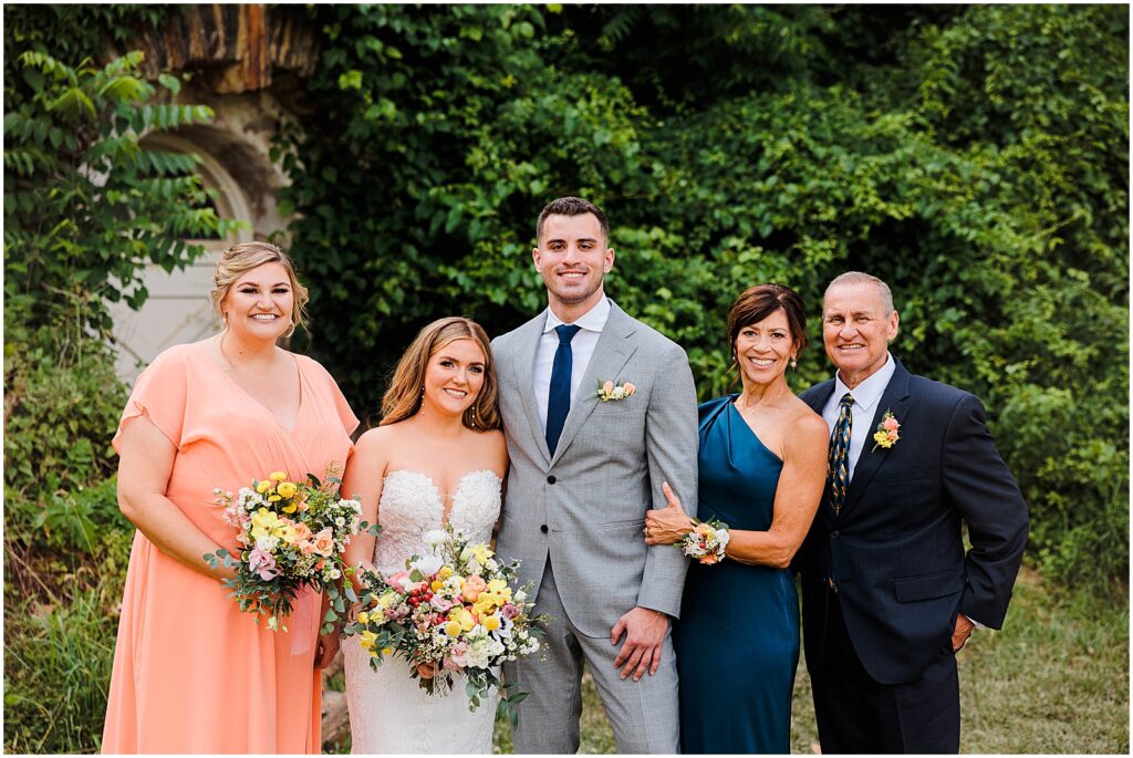 A bride and groom pose with parents and a bridesmaid.