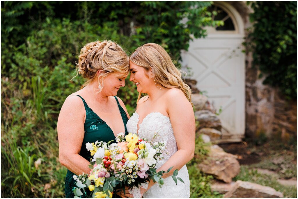 A bride touches her forehead to her mother's in a candid wedding photo.