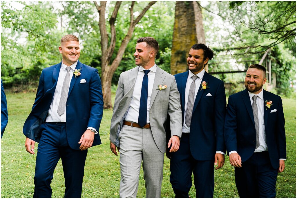 A groom walks across a lawn with his groomsmen in blue suits.