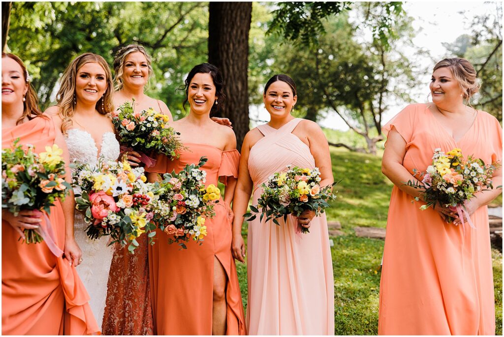 A bride poses with bridesmaids in mismatched bridesmaid dresses.