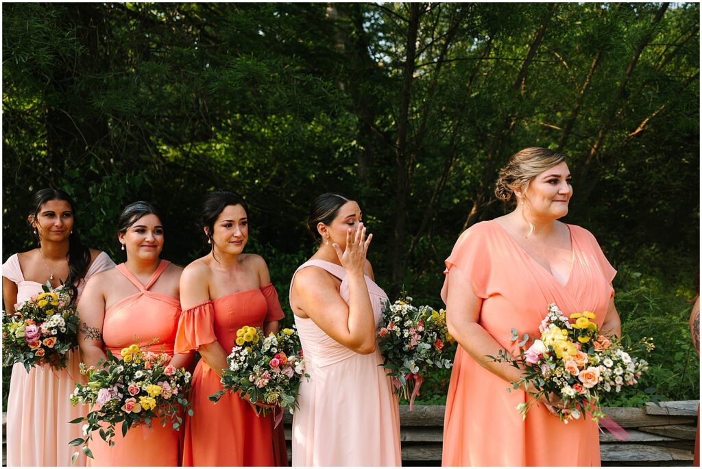 Bridesmaids in pink dresses wipe away tears during a June wedding ceremony.