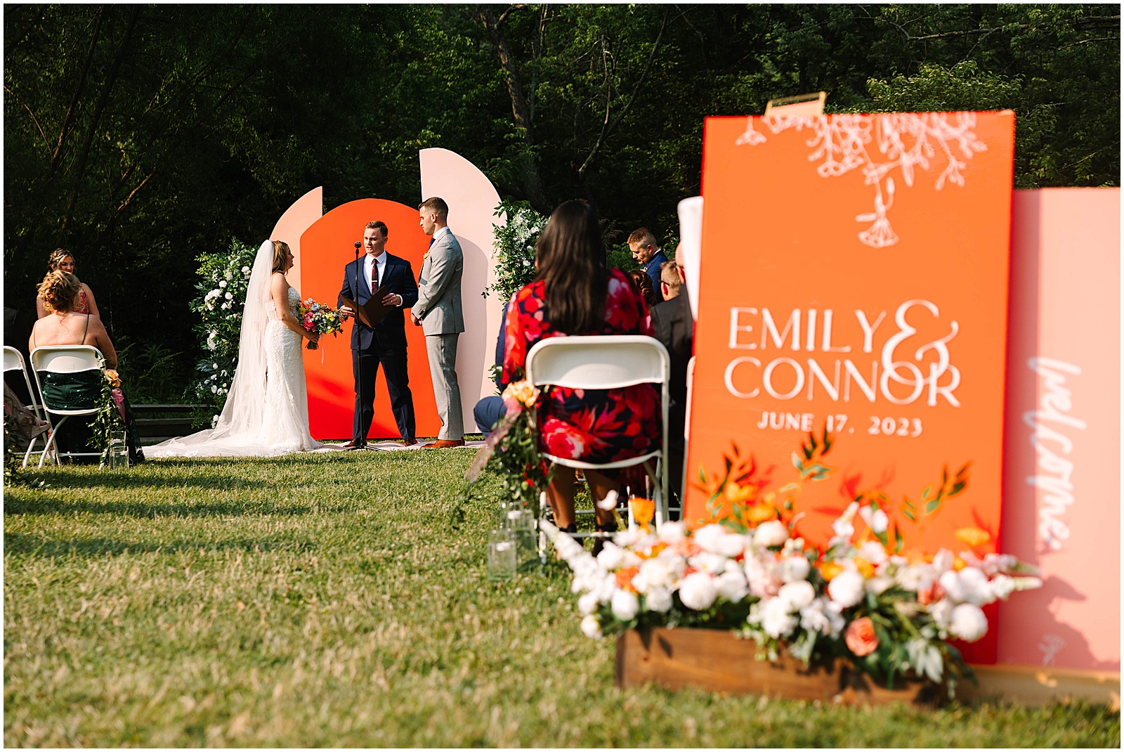 A bride and groom stand in front of an orange and pink wedding ceremony backdrop at a Philander Chase Knox Estate wedding.