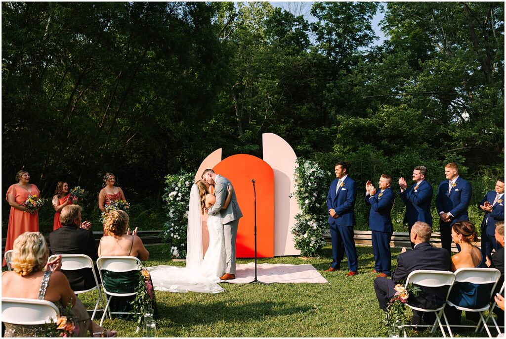A bride and groom share their first kiss at the end of their summer wedding ceremony.