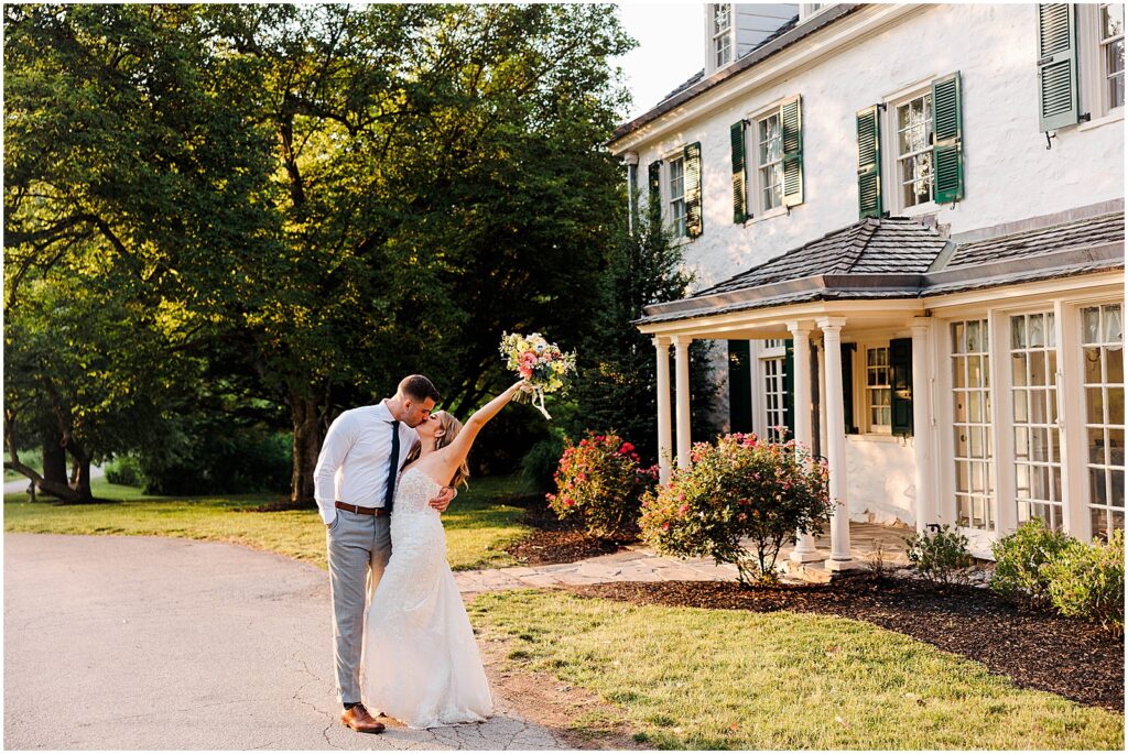 A bride and groom kiss on a path in front of the house at Philander Chase Knox Estate.