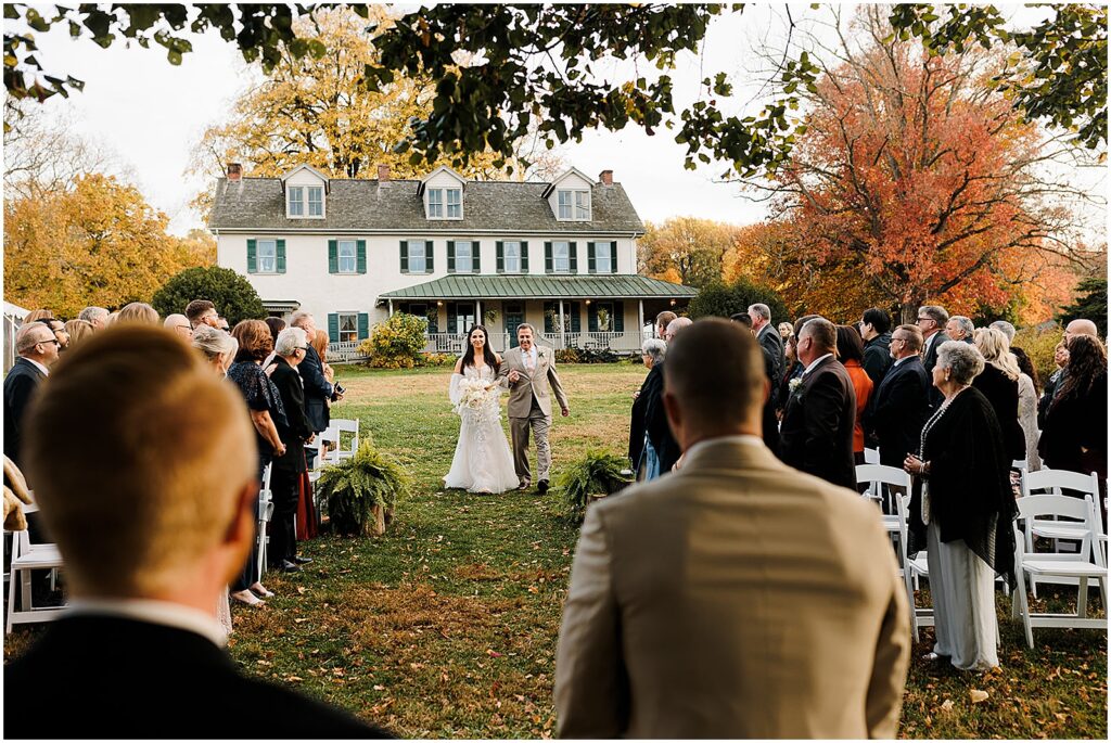 A bride's father walks her up the aisle at an outdoor wedding ceremony.