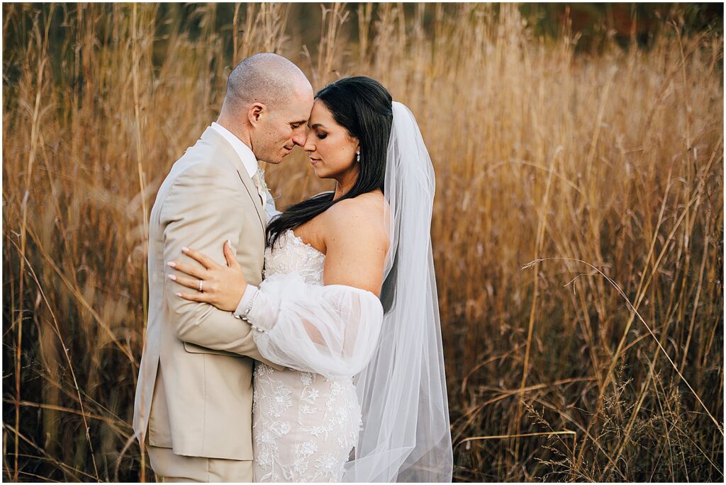 A bride and groom touch foreheads in a field for wedding photos.