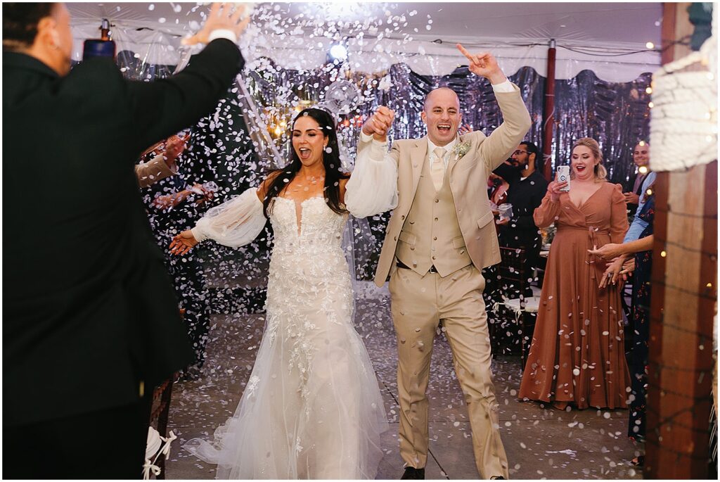 A bride and groom laugh during a confetti reception entrance.