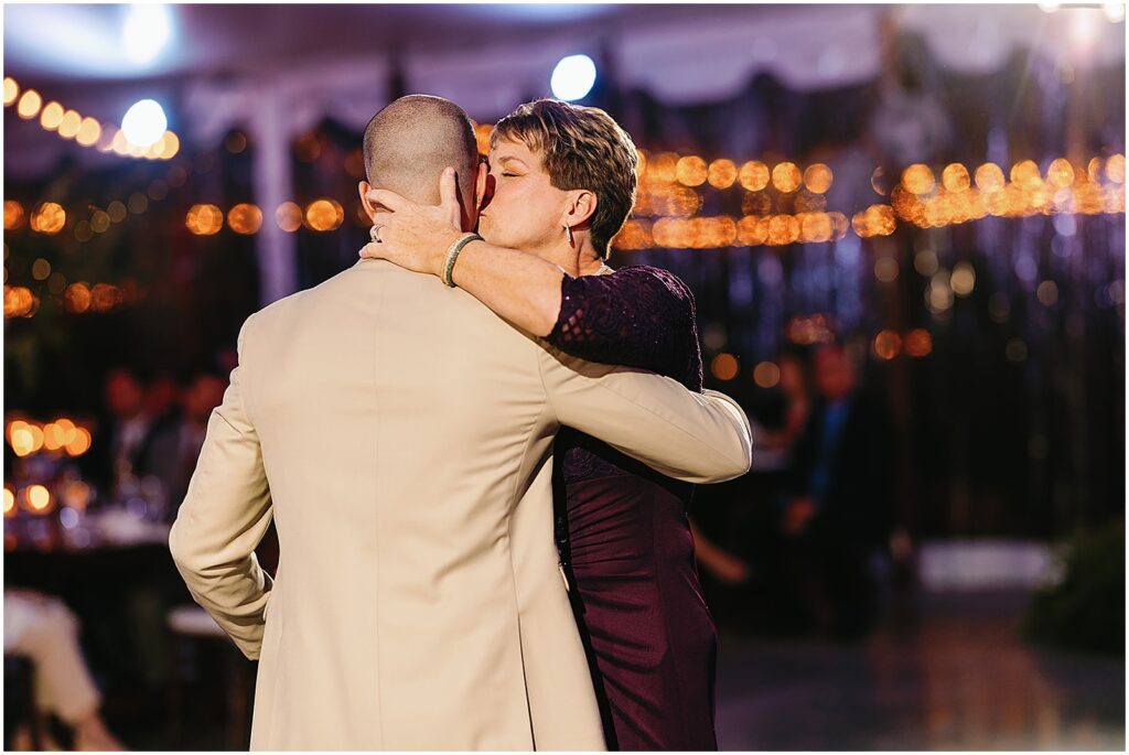 A groom's mother kisses his cheek while they dance.
