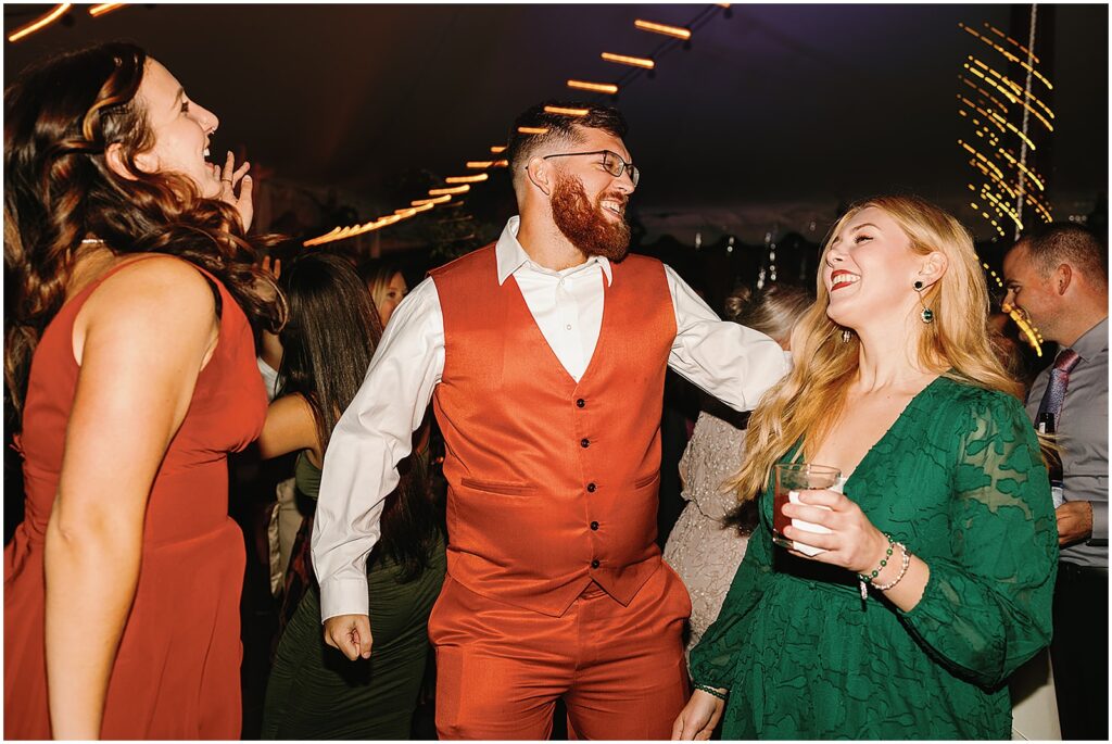 A wedding guest in an orange vest dances with other guests.