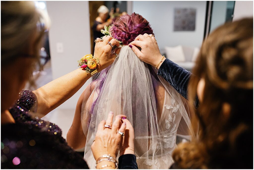 A bride's family members fasten her bridal veil on her purple hair.