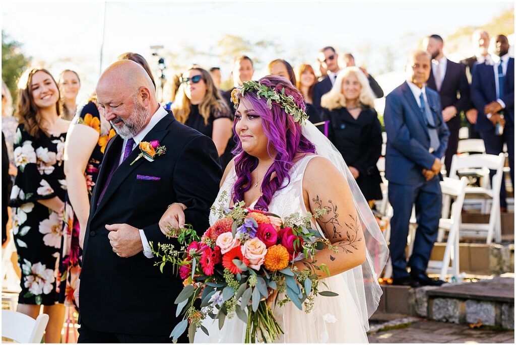 A bride's father walks her down the aisle at her outdoor wedding.