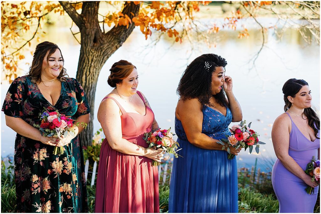 A bridesmaid wipes away a tear during a fall wedding ceremony beside a lake.