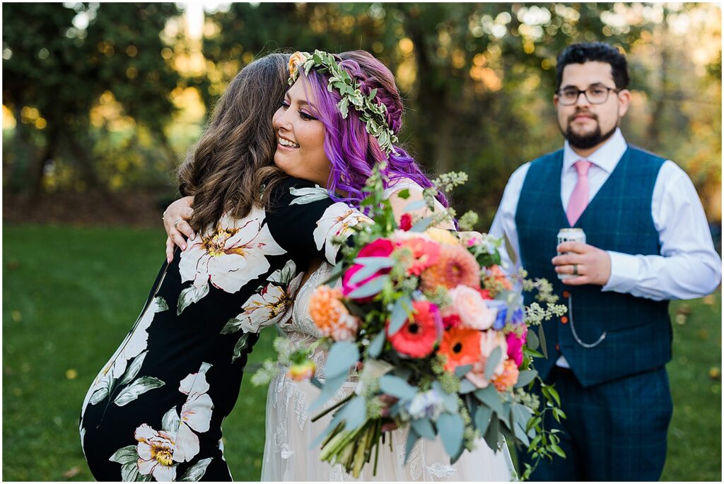A bride with purple hair hugs a friend.