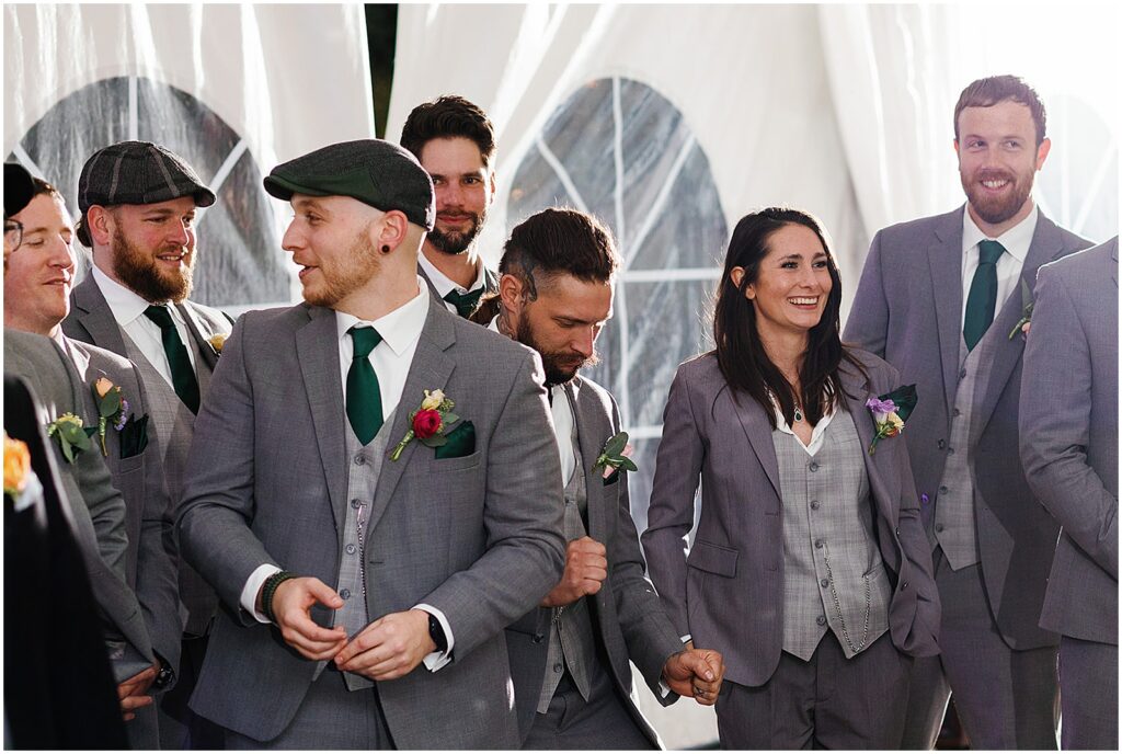 A groom's wedding party watches the first dance smiling.