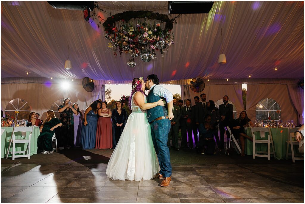 A bride and groom kiss beneath a disco ball floral installation.