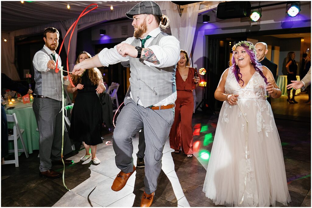 A groomsman waves a ribbon on the dance floor.