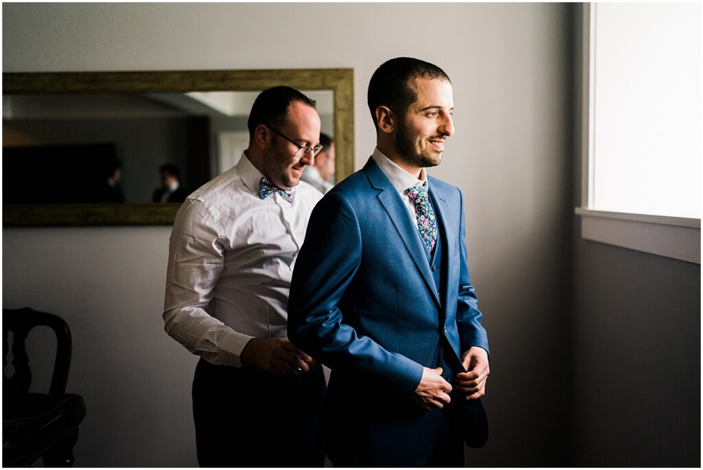 A groom's father helps him put on his jacket for a grooms portrait.