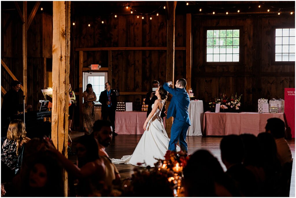 A bride and groom share a first dance as wedding guests look on.