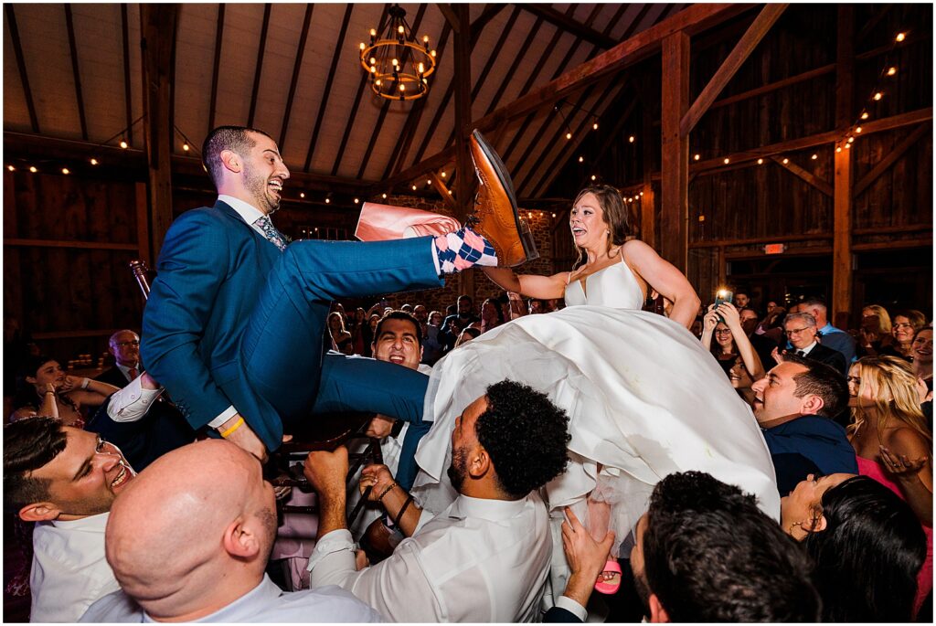 Guests lift a bride and groom on chairs for the horah.