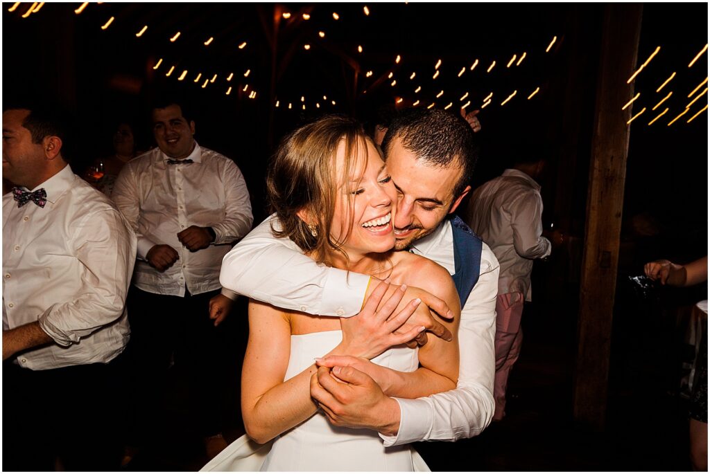 A groom wraps his arms around a bride in a white reception dress in a direct flash wedding photo.