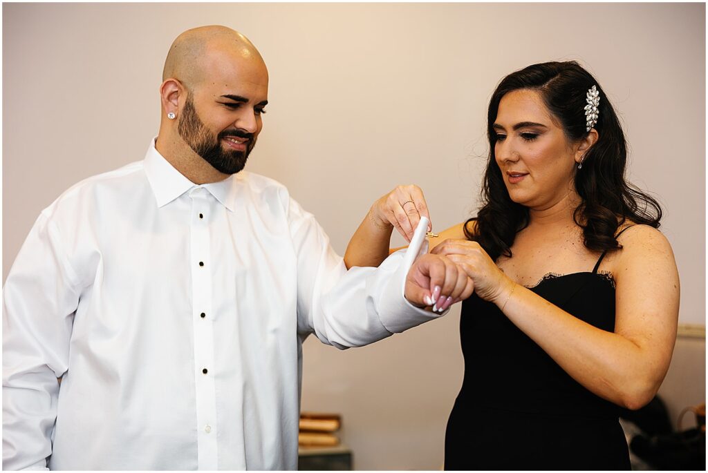 A bridesmaid fastens a groom's cufflink.