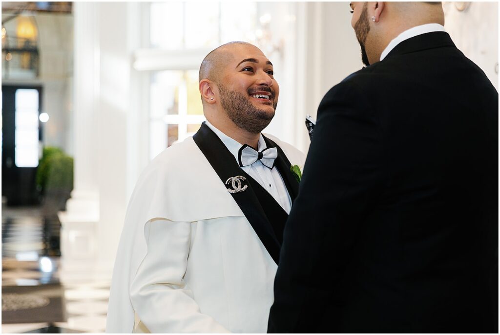 A groom wearing a Chanel brooch smiles at his husband.