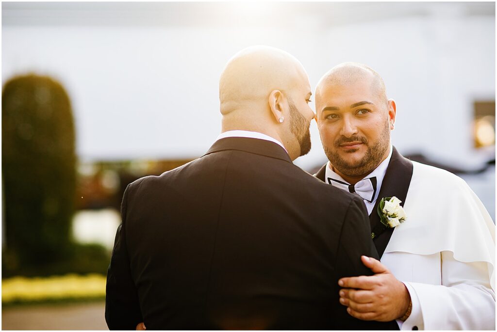 Two grooms embrace for sunset wedding photos.