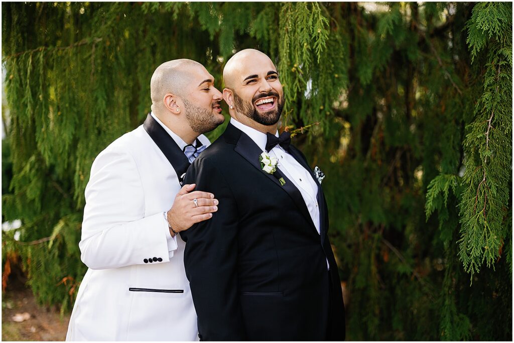 One groom leans over and whispers in the ear of another who laughs.
