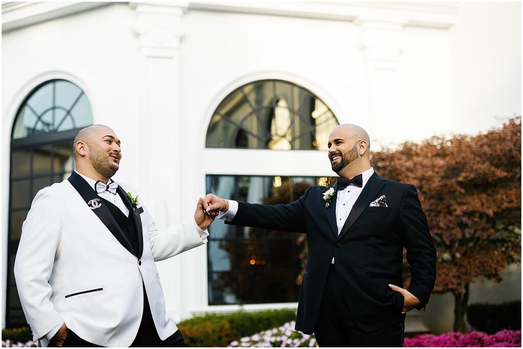 Two grooms hold hands and laugh in the courtyard of the Addison Park.