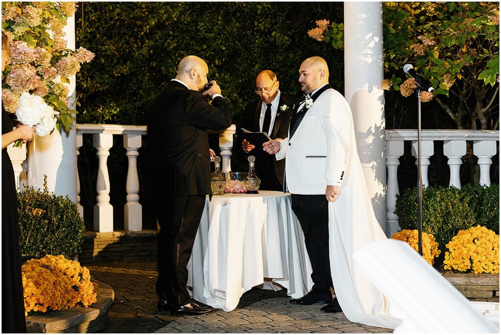 Two grooms share wine in a unity ceremony.