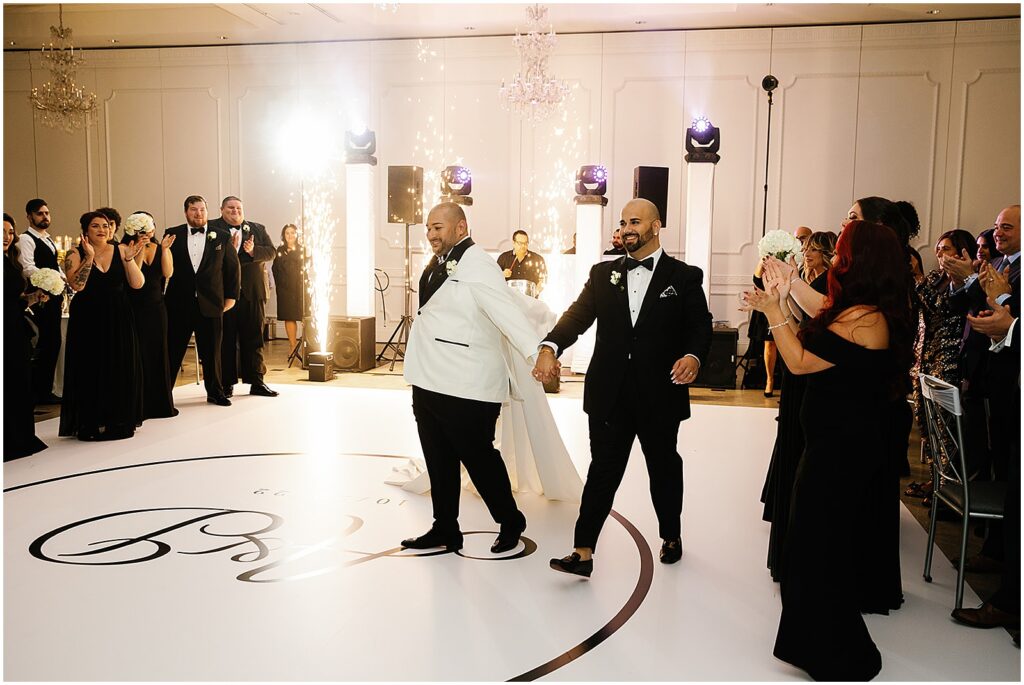 Two grooms make their reception entrance and wave to guests.