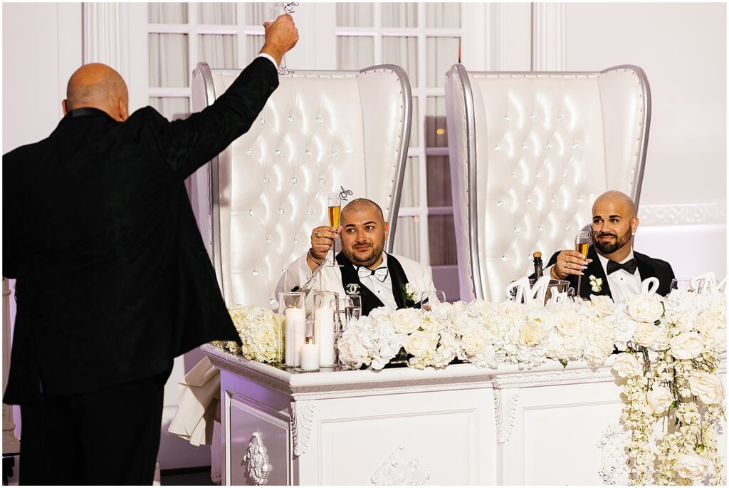 Two grooms raise their glasses after a wedding toast.