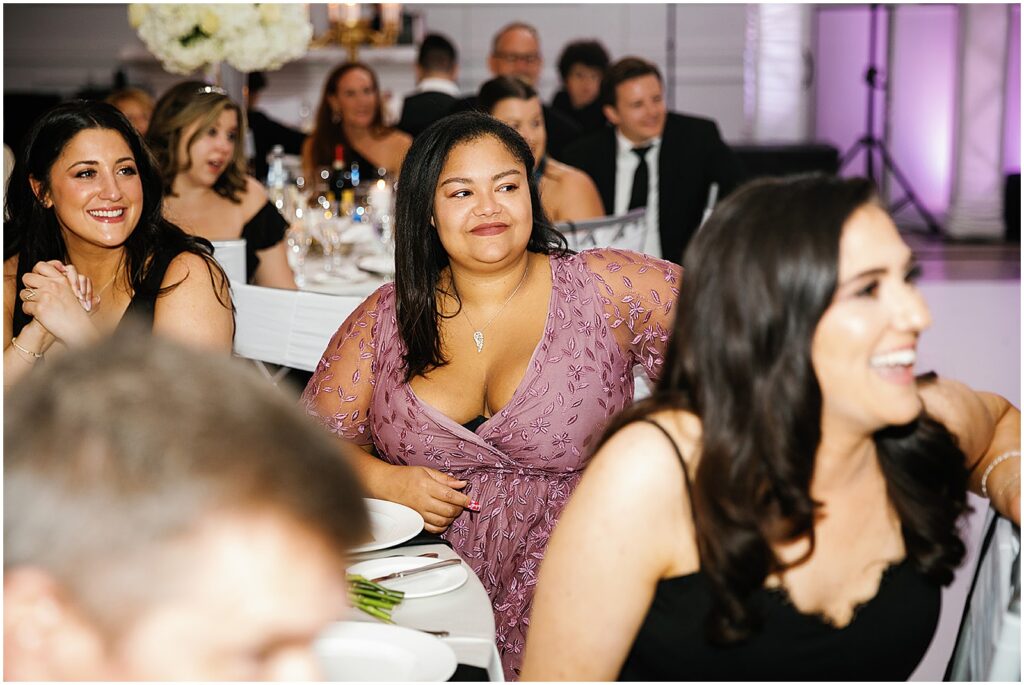 Wedding guests laugh while they watch a speech.