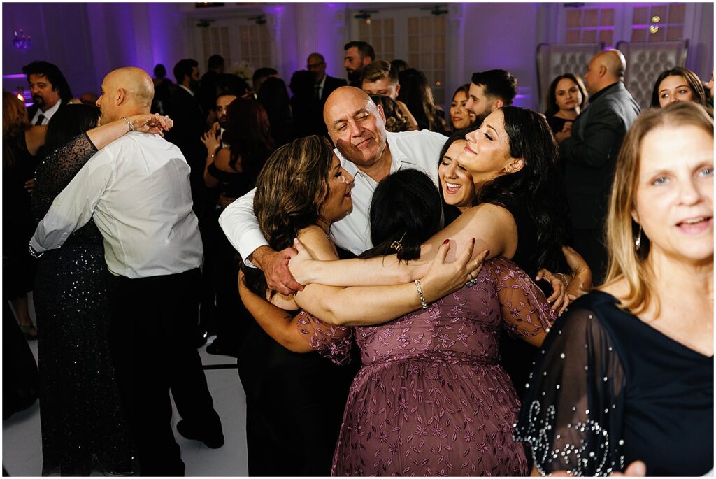 A group of wedding guests hug on a dance floor.