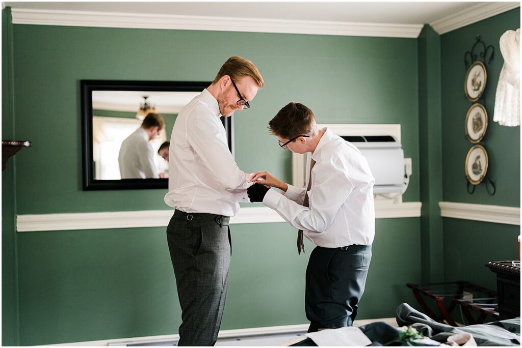 A groomsman helps a groom fasten a cufflink in a New Jersey wedding venue.