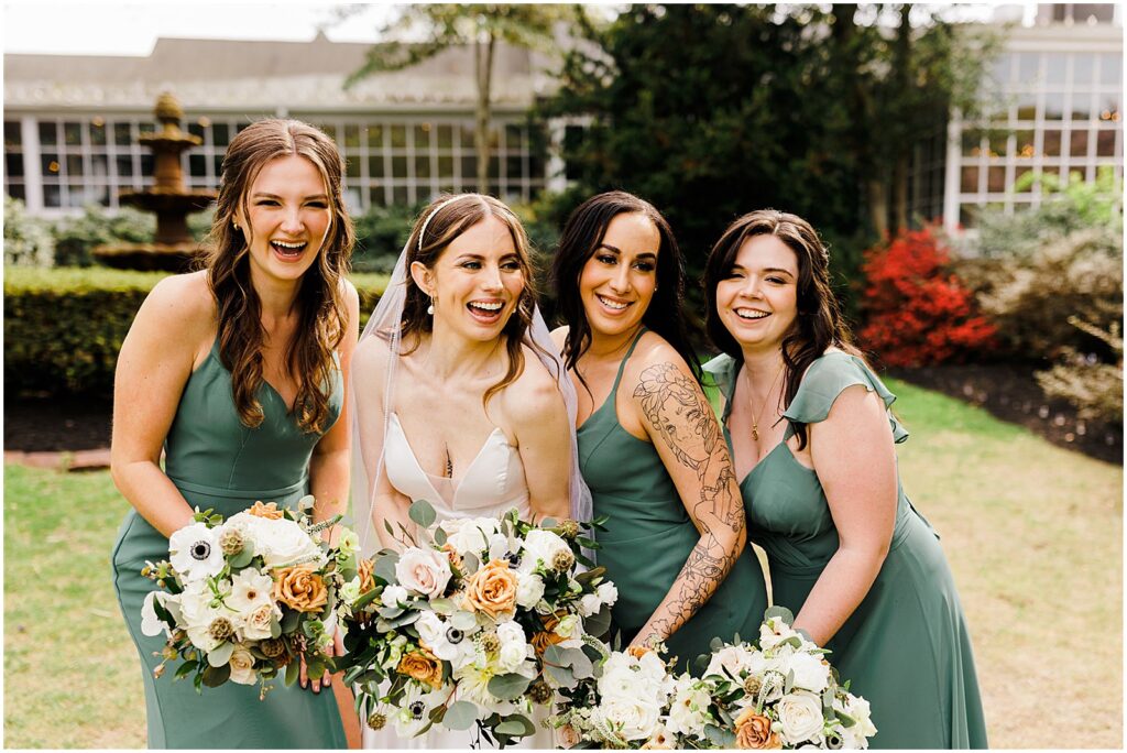 A bride laughs with her bridesmaids standing beside her for wedding party portraits.